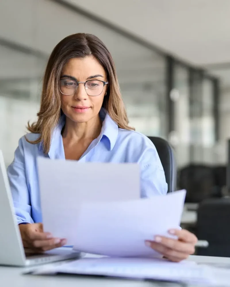 Busy business woman of middle age working on laptop checking documents. Busy business woman of middle age working on laptop checking documents.